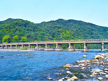 A scenic view of Arashiyama featuring the iconic Togetsukyo Bridge over the river with lush green mountains in the background.